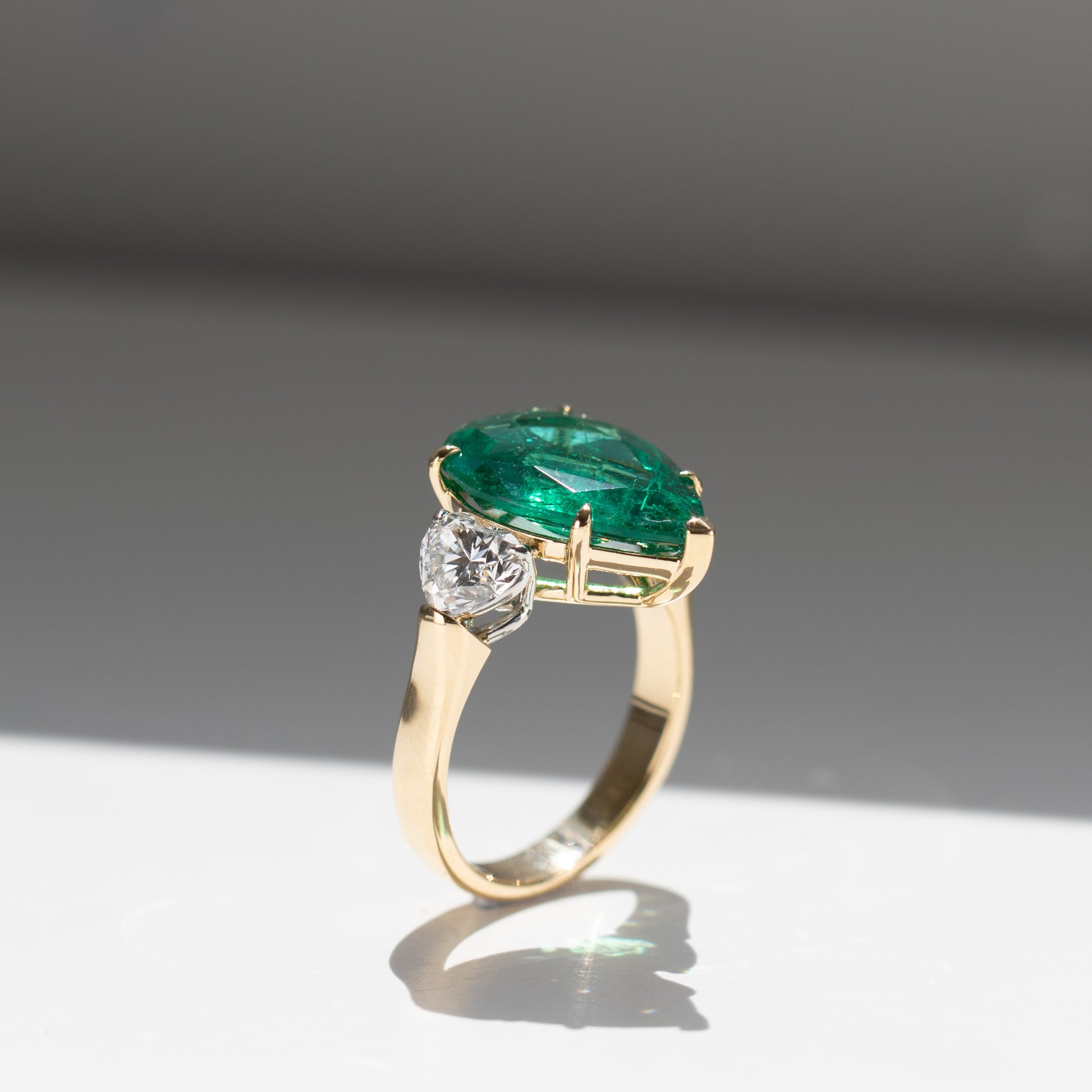 Show-stopping 5.65ct green pear cut emerald ring with heart shape diamonds in 18k gold by Valentina Fine Jewellery Hong Kong. Free global shipping including USA